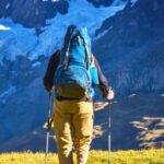 Pessoa com mochila e bast&otilde;es caminhando entre montanhas